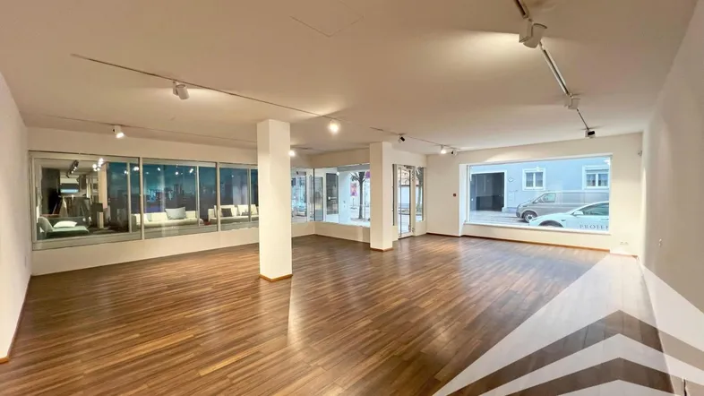 Geräumiger Geschäftsraum mit großen Schaufenstern und dunklem Laminatboden, ideal für Einzelhandel oder Büro.