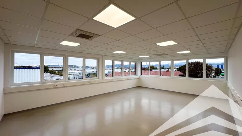 Heller, leerer Büroraum mit vielen Fenstern und Blick auf die Umgebung, ausgestattet mit Rasterdecke und Einbauleuchten.