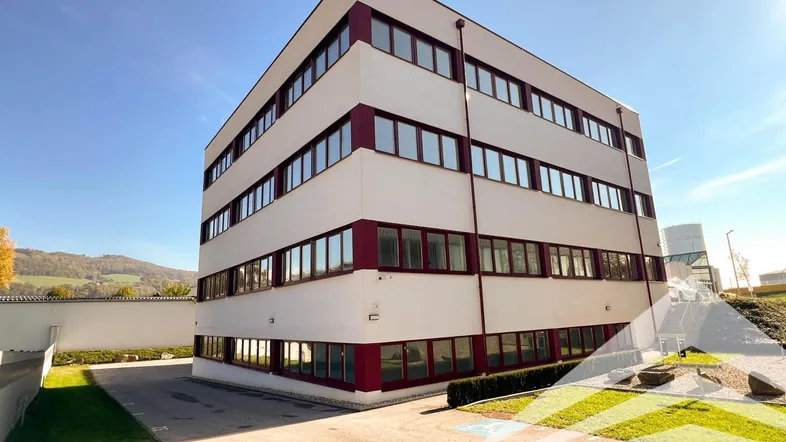 Modernes Bürogebäude mit weißer Fassade und markanten roten Fensterrahmen unter blauem Himmel.
