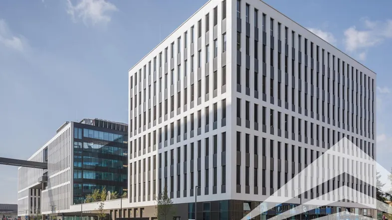 Modernes Bürogebäude mit weißer Fassade und vielen Fenstern unter blauem Himmel.