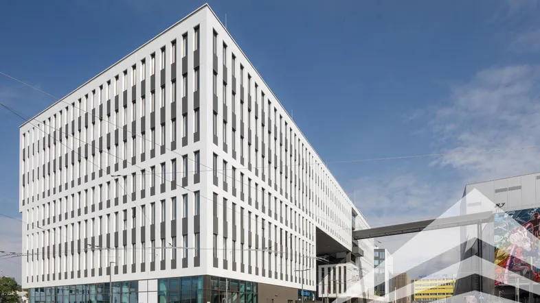 Modernes Bürogebäude mit markanter weißer Fassade und vielen vertikalen Fenstern unter blauem Himmel.
