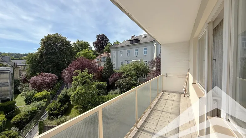 Geräumiger Balkon mit Fliesenboden und weitem Blick ins Grüne und auf umliegende Gebäude.