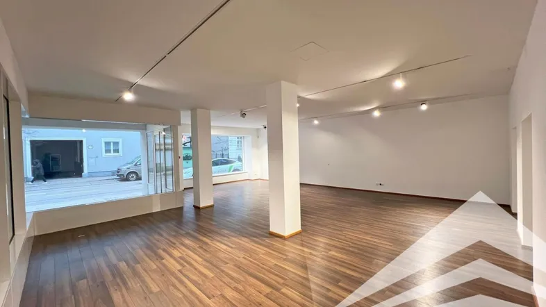 Geräumiger Geschäftsraum mit großen Schaufenstern und dunklem Holzboden, ideal für Einzelhandel oder Büro.