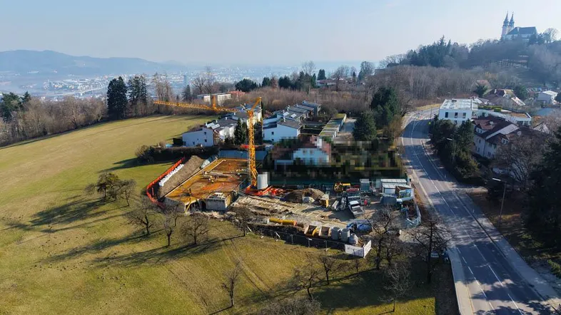 Luftaufnahme einer Baustelle mit Kran und Fundamentarbeiten für ein neues Wohngebäude in ländlicher Umgebung.