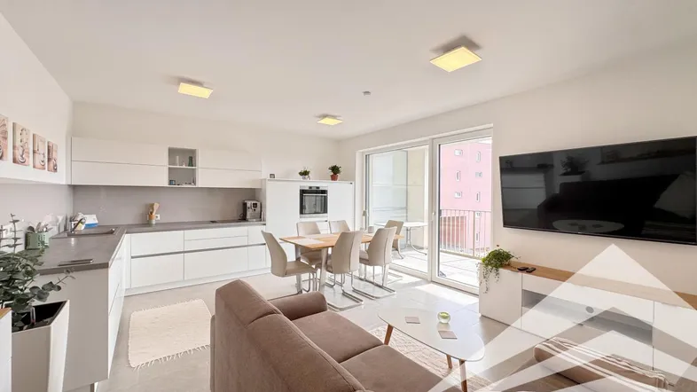 Heller offener Wohn-Essbereich mit moderner Einbauküche und Zugang zum Balkon.