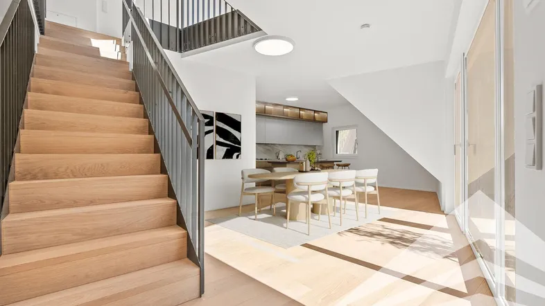 Heller offener Wohnbereich mit Holztreppe, Parkettboden und moderner Küche im Hintergrund.