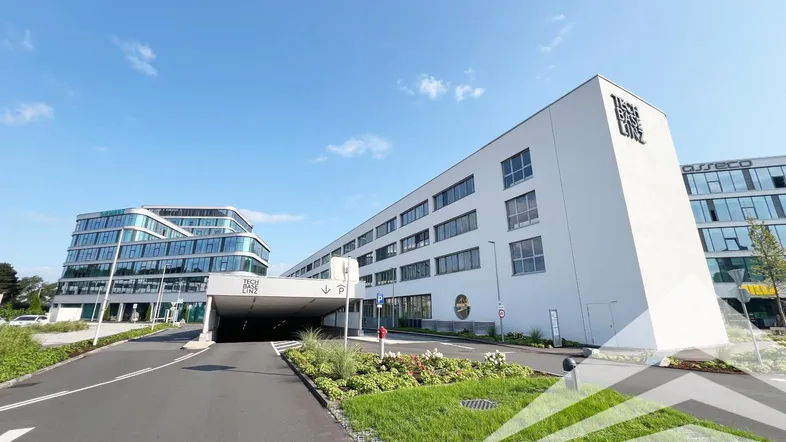 Moderne Bürogebäude mit klarer Architektur und Zufahrt zu einer Tiefgarage unter blauem Himmel.
