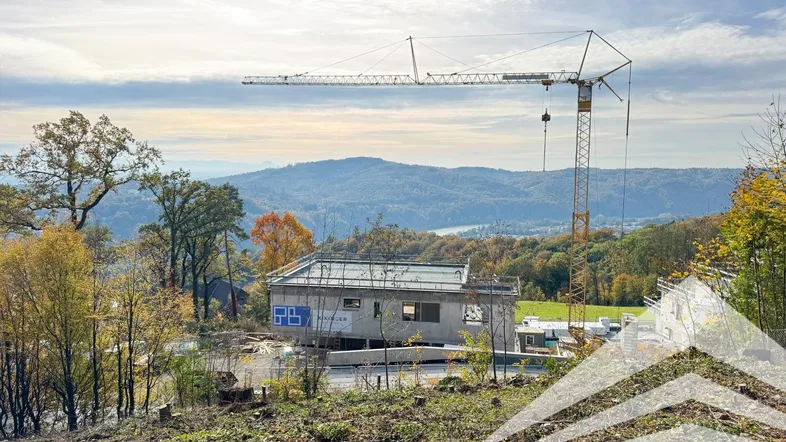 Baustelle eines Neubaus mit Kran und weitem Blick auf die umliegende Landschaft und Berge.
