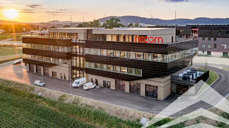 Modernes Geschäftsgebäude mit dunkler Fassade und großen Fenstern, umgeben von Feldern bei Sonnenuntergang.