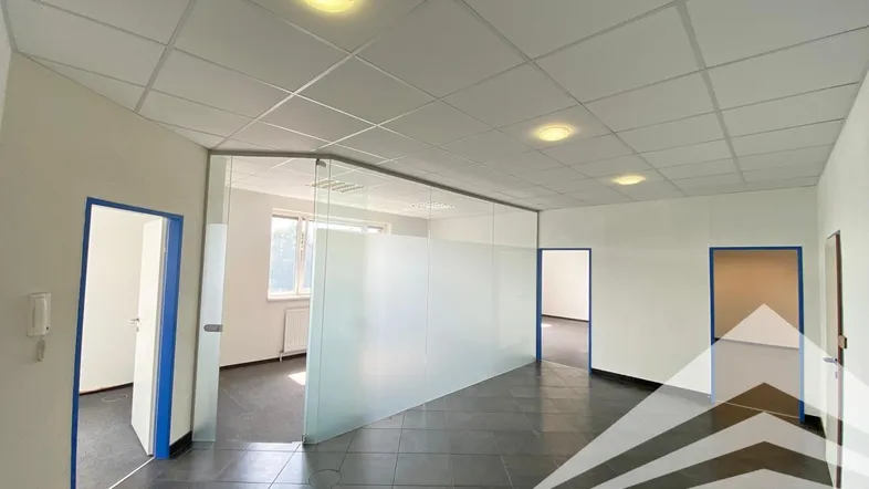 Geräumiges, leeres Büro mit dunklen Fliesen, weißen Wänden und einer modernen Glasabtrennung.