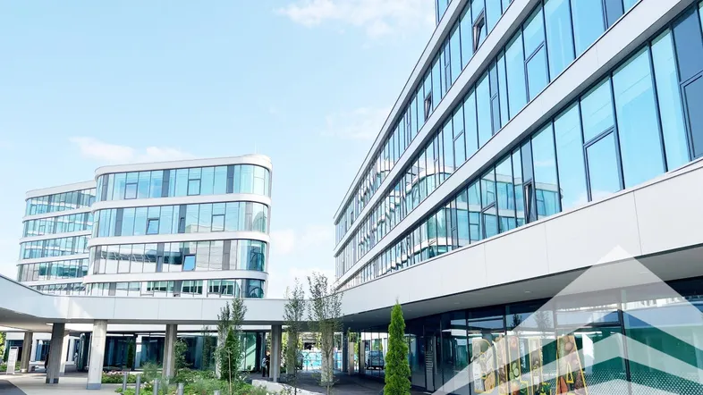 Moderne Bürogebäude mit geschwungenen Glasfassaden und gepflegten Außenanlagen unter blauem Himmel.