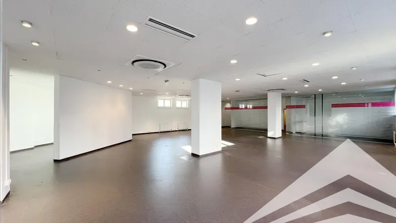 Geräumiger, leerer Geschäftsraum mit dunklem Boden und integrierter Deckenbeleuchtung, ideal für verschiedene Nutzungen.