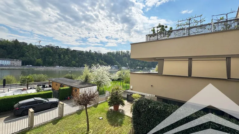 Außenansicht des modernen Gebäudes mit gepflegtem Garten und direktem Blick auf den Fluss.