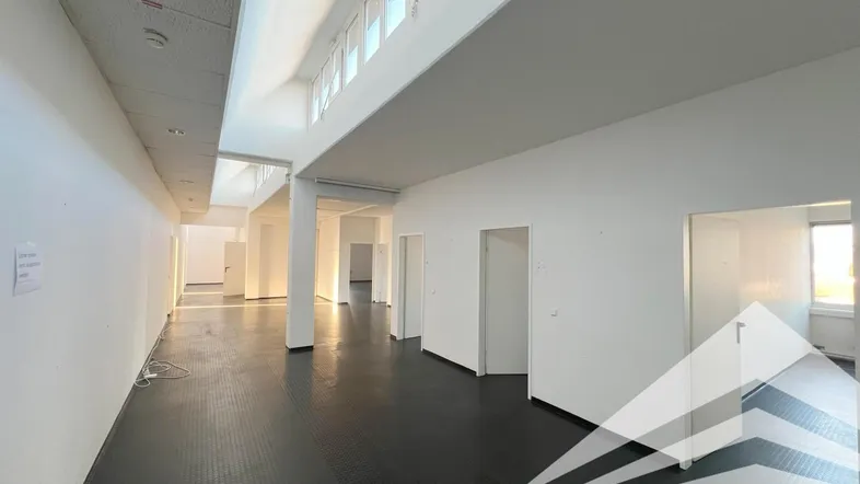 Geräumiger, leerer Büroraum mit hohen Decken und dunklem Boden, bereit für die individuelle Gestaltung.