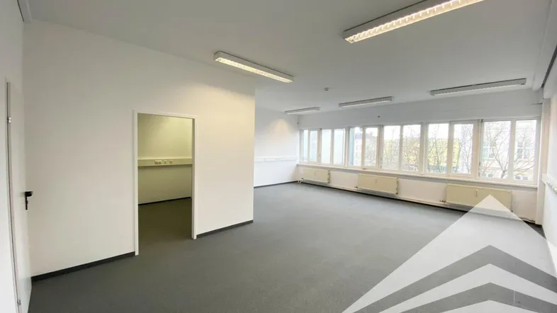 Geräumiges, leeres Büro mit Teppichboden, großen Fenstern und viel Tageslicht, bereit zur individuellen Gestaltung.