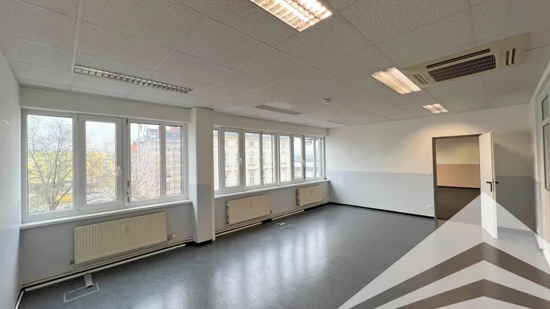 Geräumiges, leeres Büro mit großen Fenstern, grauen Böden und Deckenbeleuchtung, bereit zur Nutzung.