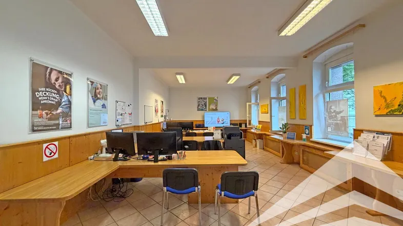 Geräumiges Büro mit mehreren Arbeitsplätzen, Holzvertäfelung und Fliesenboden, gut beleuchtet durch Fenster.
