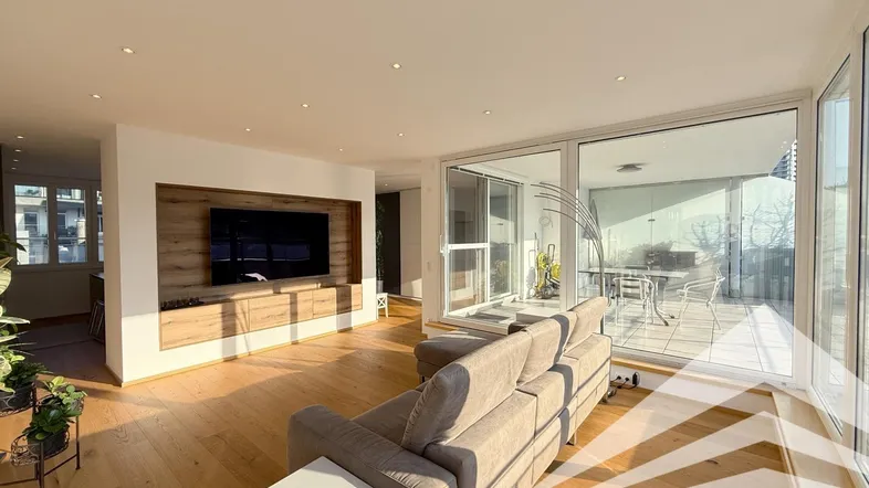 Helles Wohnzimmer mit Holzboden, integriertem TV-Bereich und Zugang zu einer sonnigen Terrasse.