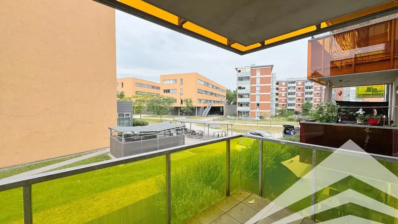 Geräumiger Balkon mit gelb-grüner Verglasung und Blick auf die umliegenden Gebäude und Grünflächen.