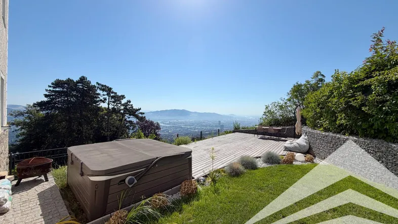 Sonniger Gartenbereich mit Whirlpool, Holzterrasse und weitem Blick über die Stadt.