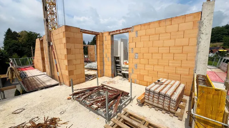 Baustelle mit im Bau befindlichen Ziegelwänden und sichtbaren Baumaterialien unter blauem Himmel.