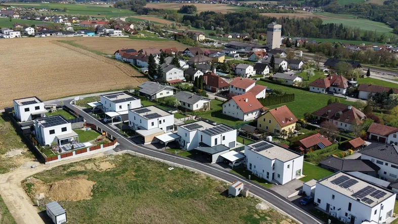 Luftaufnahme einer modernen Wohnsiedlung mit Neubauten und Photovoltaikanlagen in ländlicher Umgebung.