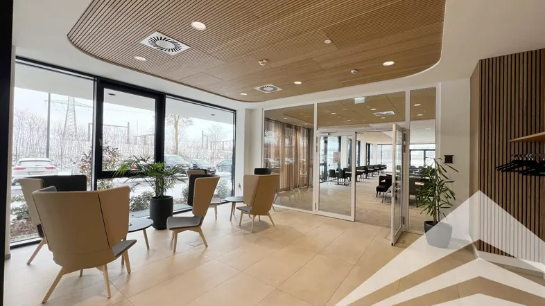 Moderner Loungebereich mit großen Fenstern, Holzlamellendecke und beigefarbenen Fliesenböden, ideal für Empfangsbereiche.
