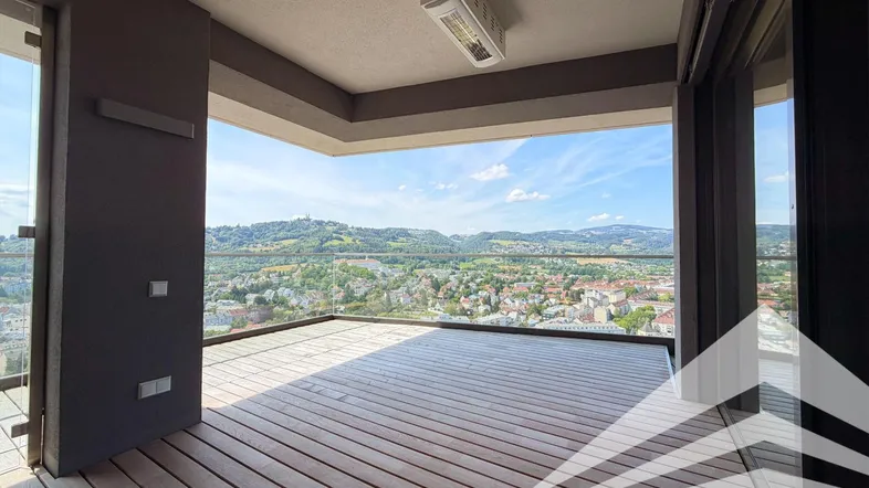 Geräumige Terrasse mit Holzboden, Glasgeländer und weitem Blick über die Stadt und grüne Hügel.