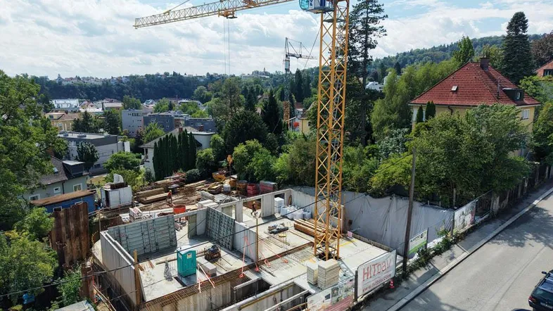 Baustelle eines Neubaus mit Kran, Fundament und ersten Mauern in grüner Umgebung.