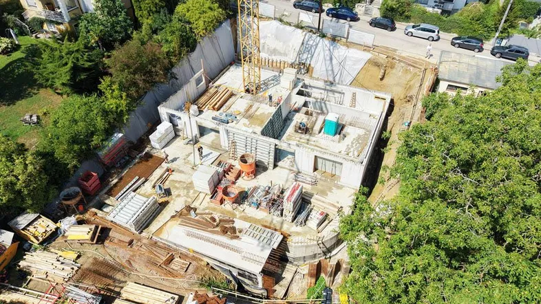 Luftaufnahme einer Baustelle mit Kran und bereits errichteten Fundamenten für ein neues Gebäude.