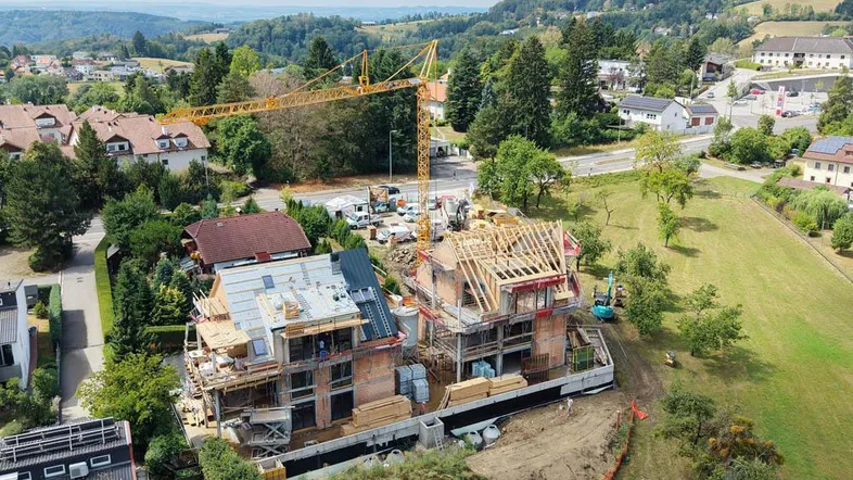 Luftaufnahme einer Baustelle mit zwei im Bau befindlichen Gebäuden und einem Kran in ländlicher Umgebung.