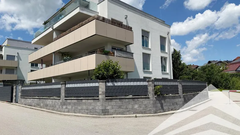 Modernes Mehrfamilienhaus mit mehreren Balkonen und einer gepflegten Außenanlage unter blauem Himmel.