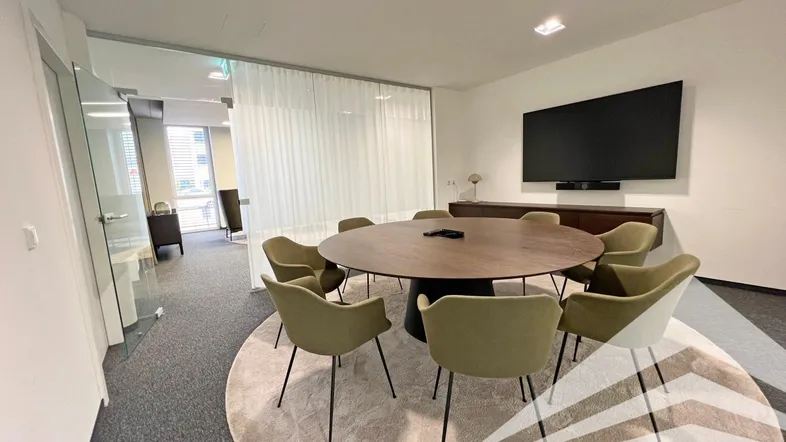 Moderner Besprechungsraum mit großem runden Tisch, bequemen Stühlen und integriertem Bildschirm für Präsentationen.