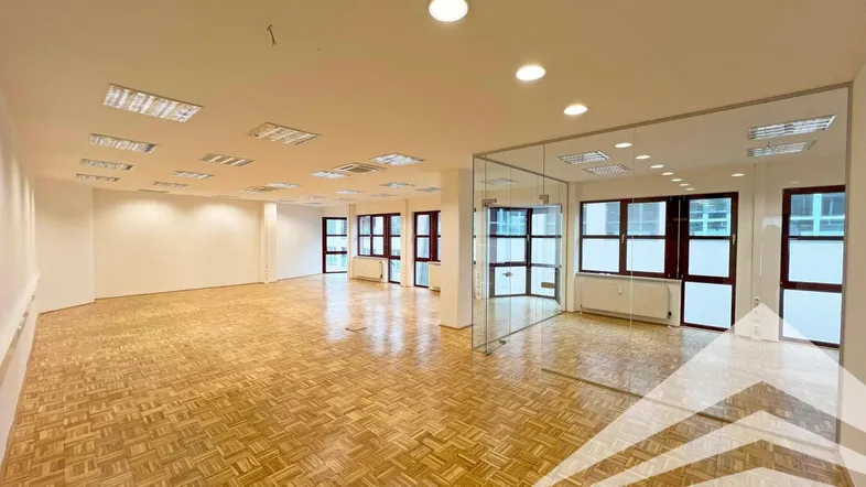 Geräumiges und helles Büro mit Parkettboden, großen Fenstern und moderner Glasabtrennung.
