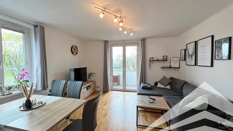 Heller Wohn- und Essbereich mit Holzboden, gemütlichem Sofa und Zugang zum Balkon.