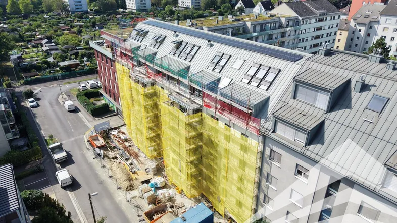 Luftaufnahme eines im Bau befindlichen Gebäudes mit Gerüst und umliegender Stadtlandschaft.
