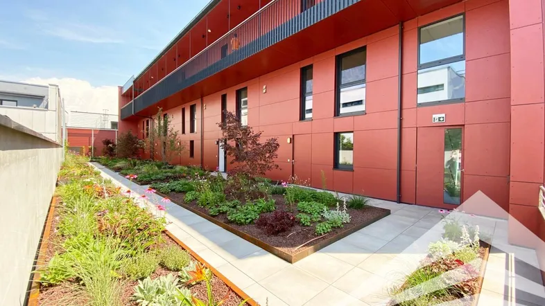 Moderne Wohnanlage mit roter Fassade und schön angelegtem Gartenbereich im Freien.