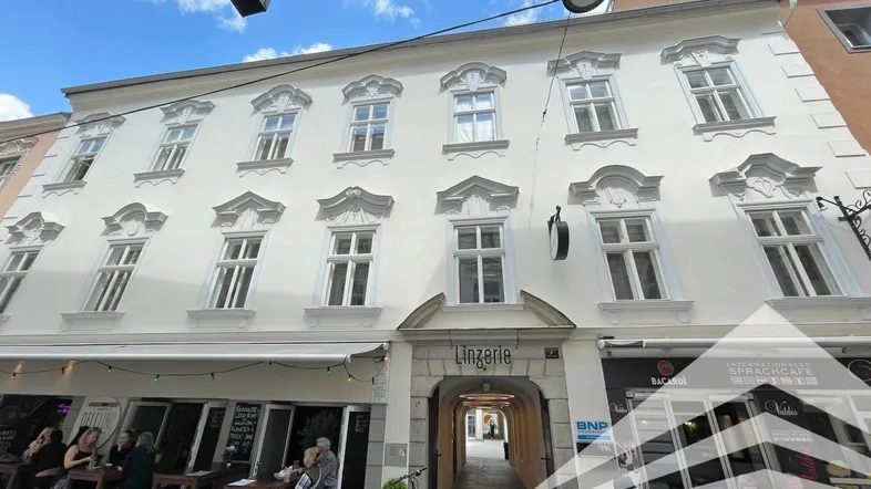 Historisches Gebäude mit weißer Fassade und Geschäften im Erdgeschoss in einer belebten Straße.