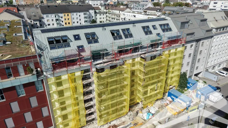 Luftaufnahme eines im Bau befindlichen Gebäudes mit Gerüst und Solarmodulen auf dem Dach.