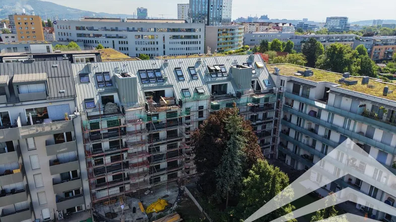 Luftaufnahme eines im Bau befindlichen Gebäudes mit Gerüst und umliegender Stadtlandschaft.