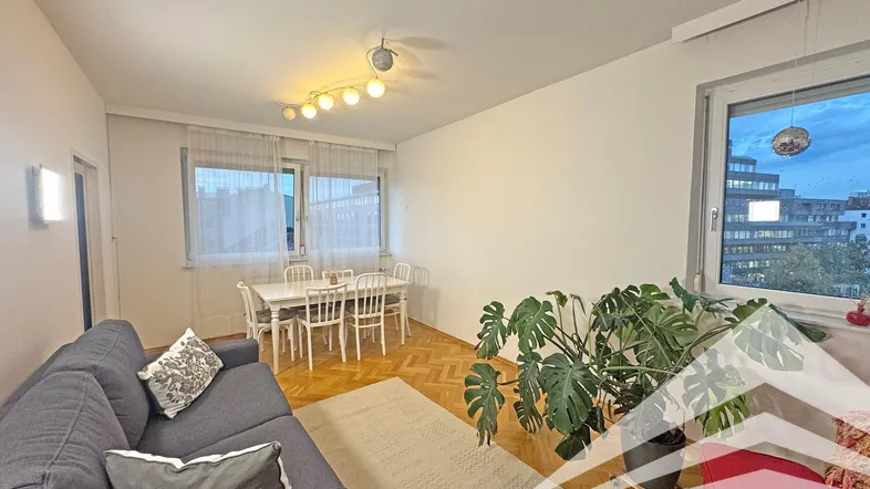 Helles Wohn- und Esszimmer mit Parkettboden, bequemer Couch und Esstisch für mehrere Personen.