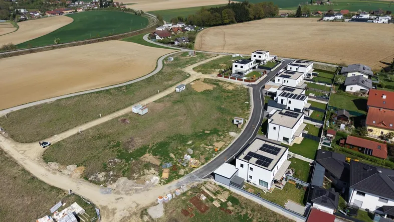 Luftaufnahme einer neuen Wohnsiedlung mit modernen Häusern und Photovoltaikanlagen in ländlicher Umgebung.