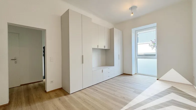 Helles Zimmer mit modernem Einbauschrank, hellem Laminatboden und großem Fenster.