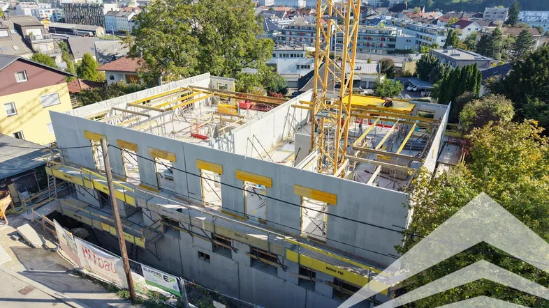 Luftaufnahme einer Baustelle mit Kran und im Bau befindlichem Gebäude in städtischer Umgebung.