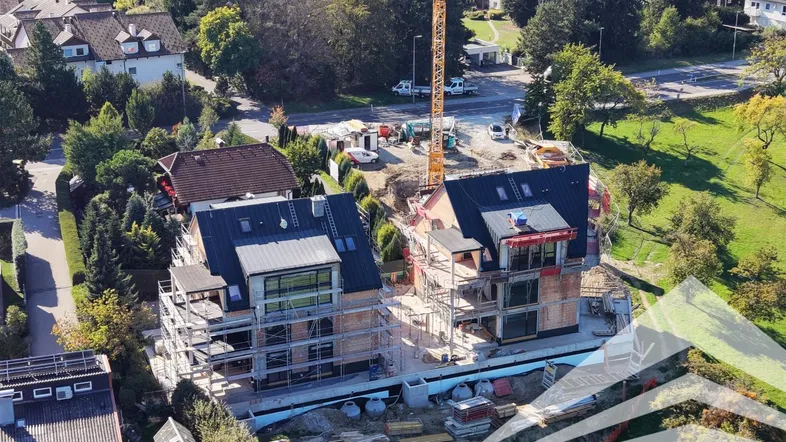 Luftaufnahme von zwei im Bau befindlichen Wohnhäusern mit Gerüst und Kran in grüner Umgebung.