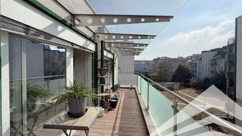 Heller Balkon mit Holzboden, Glasgeländer und Überdachung, bietet einen weiten Blick über die Stadt.