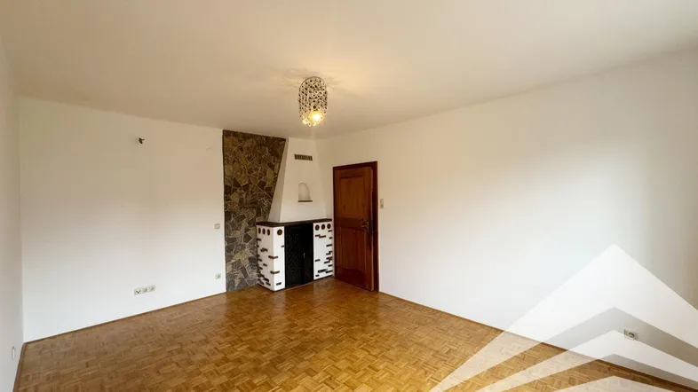 Geräumiges Wohnzimmer mit Parkettboden, einem dekorativen Kamin und einer Holztür.