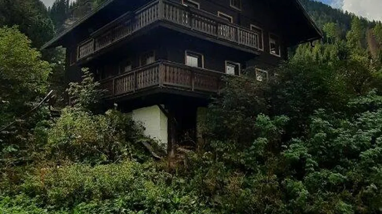 Traditionelles Holzhaus in den Bergen mit mehreren Balkonen und grüner Umgebung unter bewölktem Himmel.