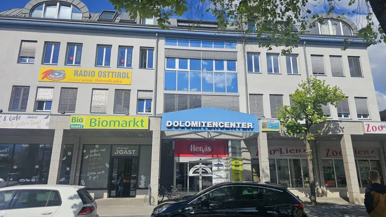 Vorderansicht eines Geschäftsgebäudes mit verschiedenen Ladenfronten und Büros im oberen Bereich.