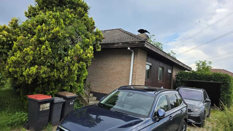Einfamilienhaus mit Ziegelfassade, Satteldach und geparkten Autos auf der Auffahrt.